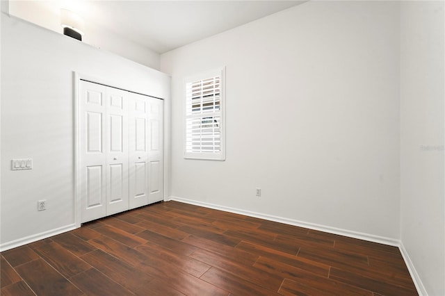 unfurnished bedroom with dark wood-style flooring, a closet, and baseboards