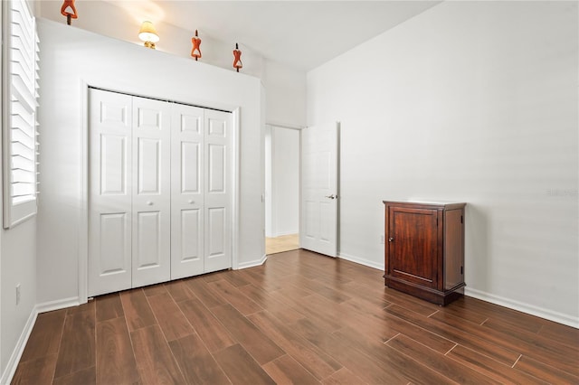 unfurnished bedroom featuring dark wood-style floors, a closet, multiple windows, and baseboards