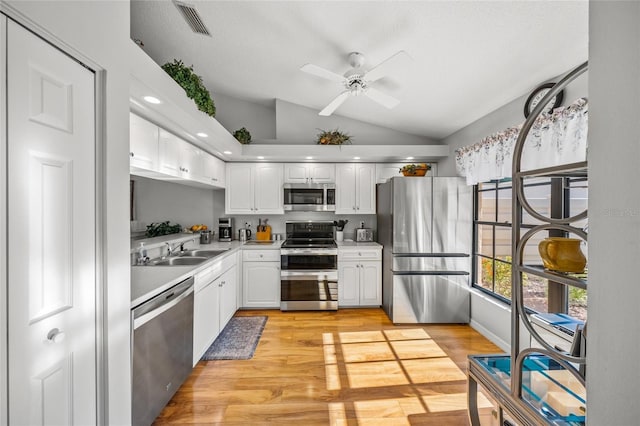 kitchen featuring stainless steel appliances, lofted ceiling, sink, and white cabinets