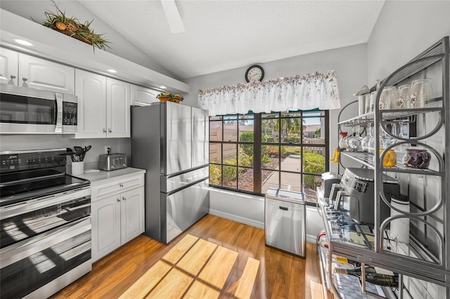 kitchen with lofted ceiling, stainless steel appliances, a textured ceiling, white cabinets, and light wood-type flooring