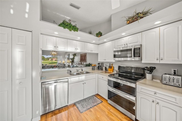 kitchen with white cabinetry, stainless steel appliances, sink, and light wood-type flooring