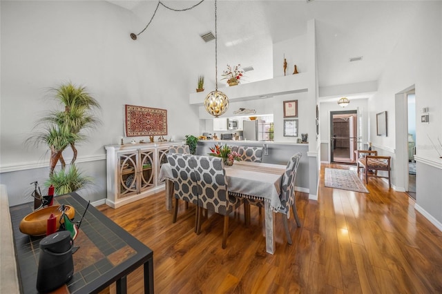 dining area with a high ceiling, hardwood / wood-style floors, and an inviting chandelier