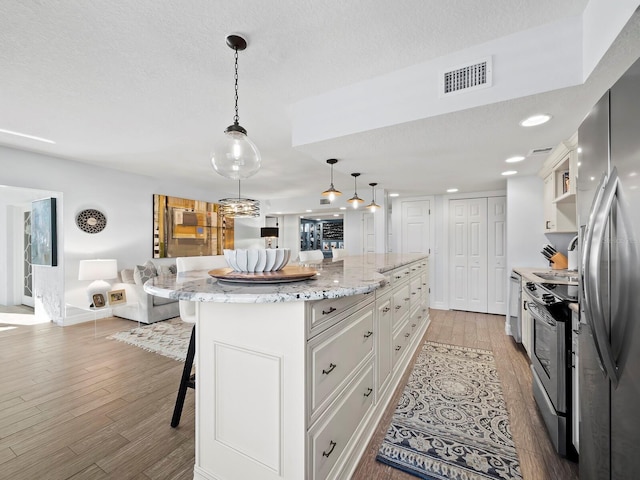 kitchen with a breakfast bar area, white cabinetry, light stone counters, decorative light fixtures, and appliances with stainless steel finishes