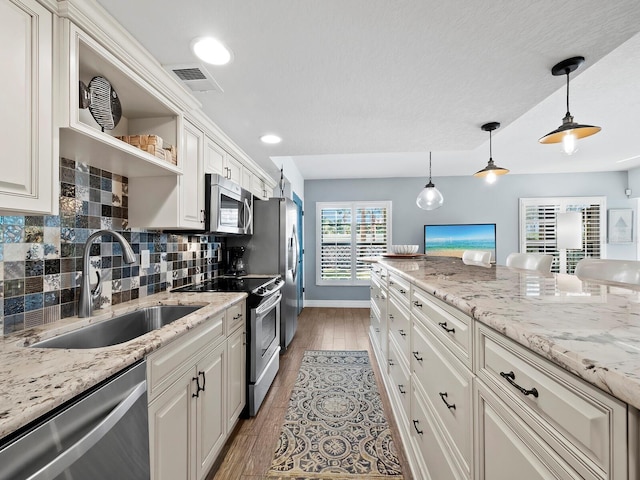 kitchen with pendant lighting, stainless steel appliances, light stone countertops, and sink