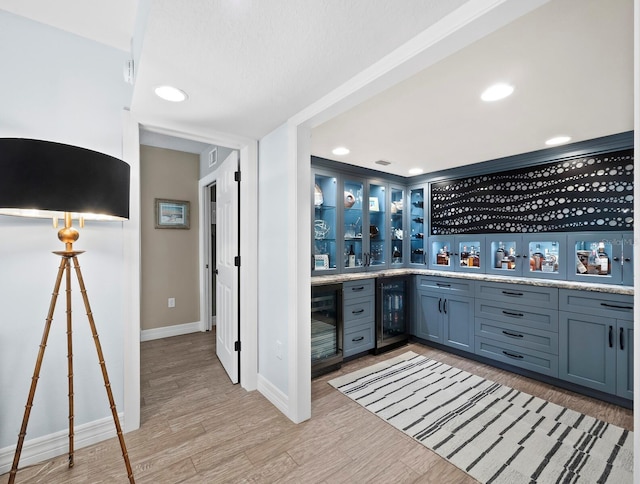 bar with wine cooler, blue cabinetry, and light hardwood / wood-style flooring