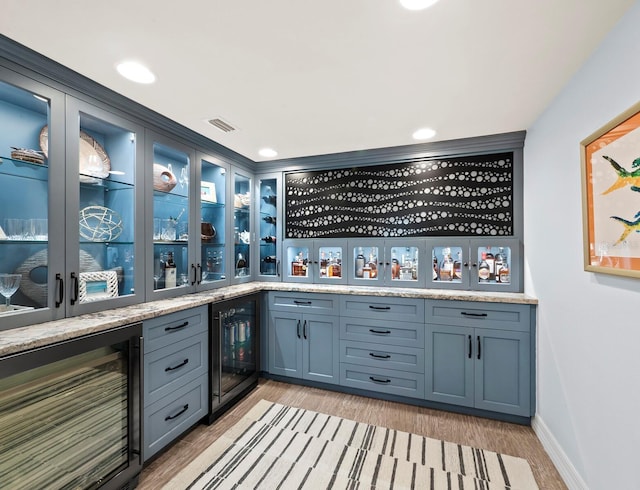 bar with light stone countertops, wine cooler, and light hardwood / wood-style flooring