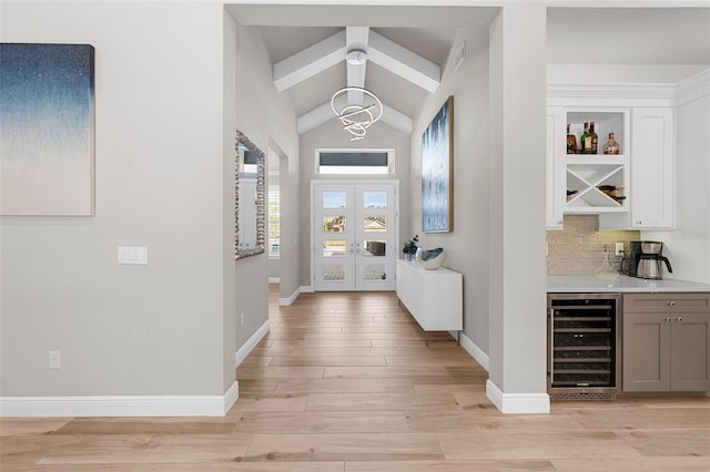 entrance foyer featuring lofted ceiling with beams, light wood-type flooring, indoor bar, a notable chandelier, and beverage cooler