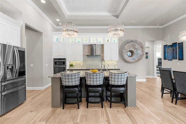 kitchen featuring stainless steel appliances, wall chimney range hood, a center island with sink, and white cabinets