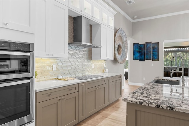 kitchen featuring white cabinets, stainless steel double oven, black electric stovetop, crown molding, and wall chimney range hood