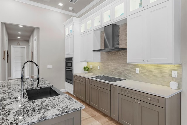 kitchen with black electric stovetop, white cabinets, sink, and wall chimney exhaust hood