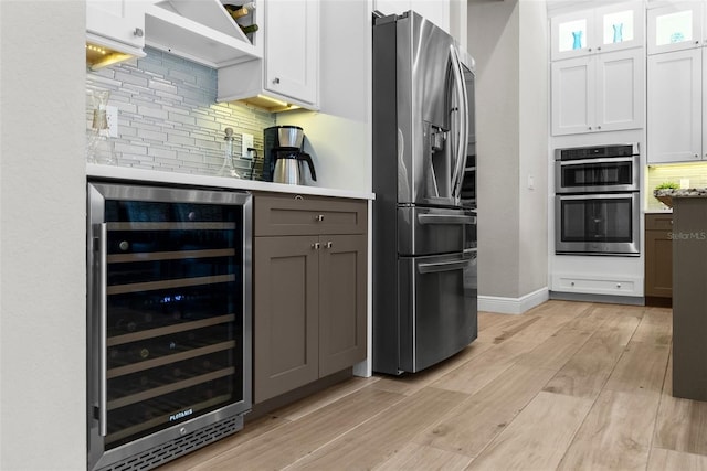 kitchen featuring white cabinets, appliances with stainless steel finishes, beverage cooler, and light hardwood / wood-style flooring