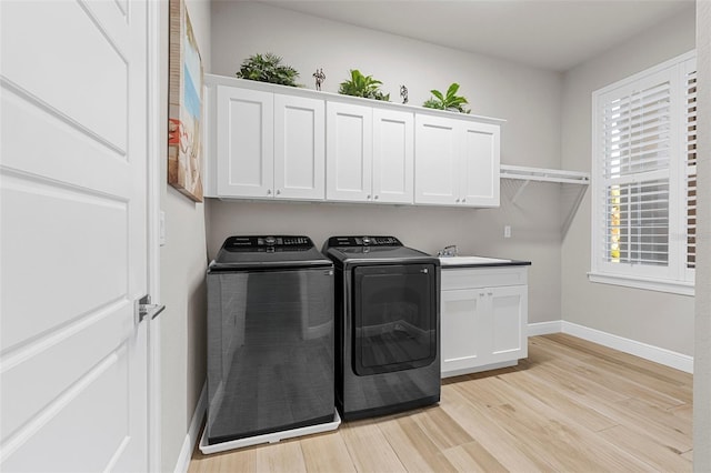 clothes washing area featuring light hardwood / wood-style floors, sink, washing machine and dryer, and cabinets