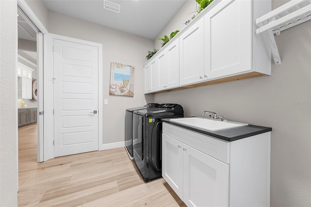 clothes washing area featuring cabinets, separate washer and dryer, sink, and light hardwood / wood-style flooring