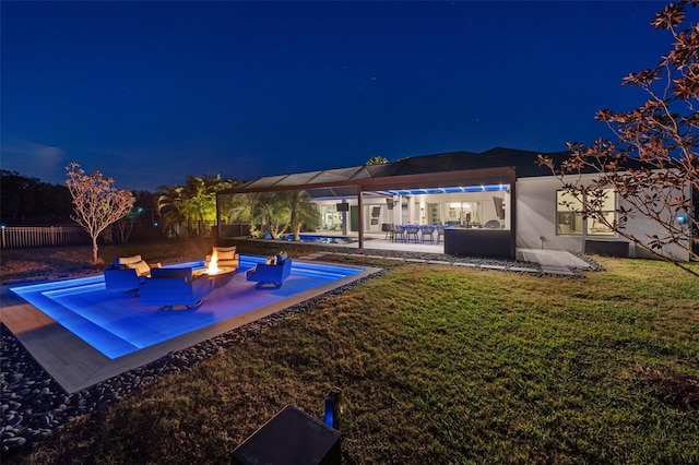 pool at night featuring an outdoor fire pit, a patio area, and a lawn