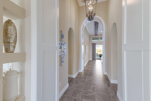 hallway featuring an inviting chandelier, a towering ceiling, and dark tile patterned flooring