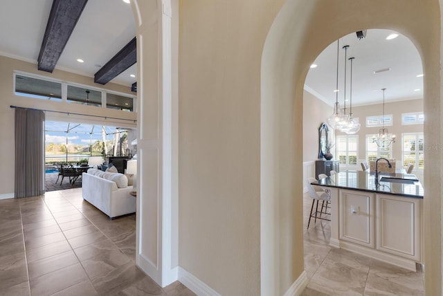 hall with ornamental molding, beam ceiling, a chandelier, and sink