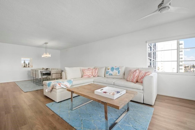 living room with ceiling fan with notable chandelier and light hardwood / wood-style flooring