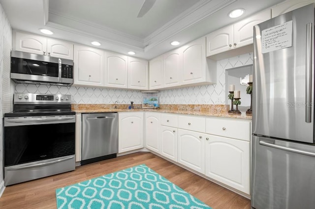 kitchen with appliances with stainless steel finishes, white cabinetry, light stone counters, crown molding, and light hardwood / wood-style flooring