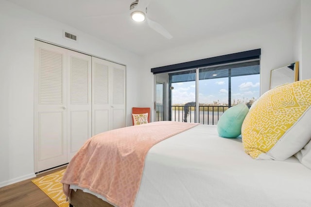 bedroom with wood-type flooring, access to outside, ceiling fan, a water view, and a closet