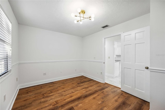 spare room with dark hardwood / wood-style floors, a wealth of natural light, and an inviting chandelier