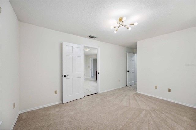 carpeted empty room featuring a chandelier and a textured ceiling