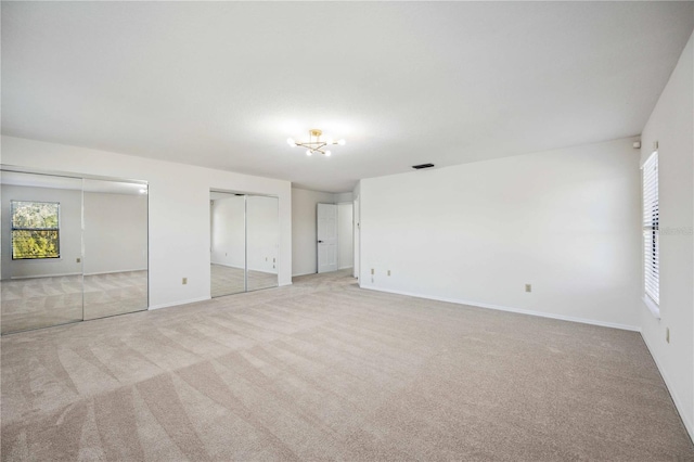 unfurnished bedroom featuring light carpet and two closets