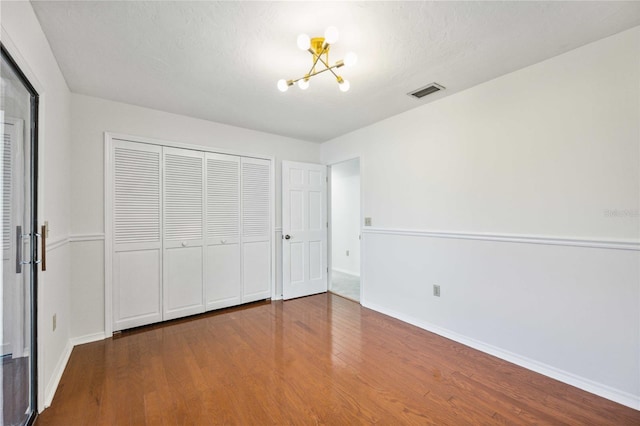 unfurnished bedroom with wood-type flooring, a closet, and a notable chandelier