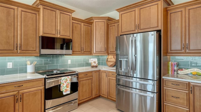 kitchen with light tile patterned floors, appliances with stainless steel finishes, light stone countertops, a textured ceiling, and decorative backsplash