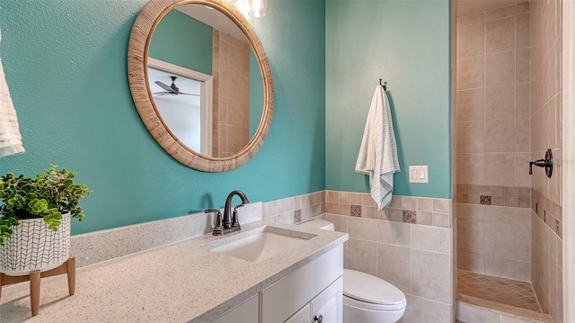 bathroom with tile walls, vanity, toilet, and tiled shower