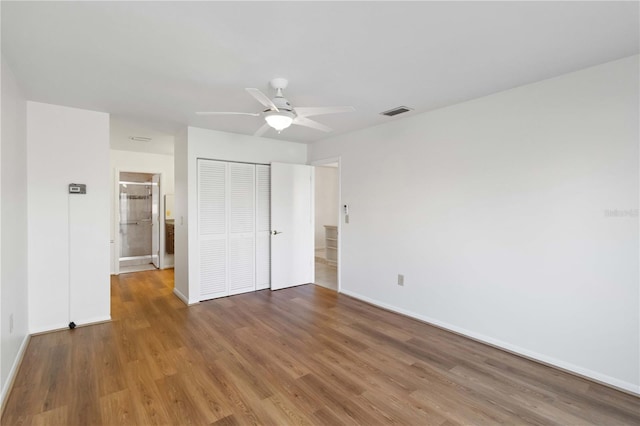 unfurnished bedroom with ensuite bath, hardwood / wood-style floors, ceiling fan, and a closet