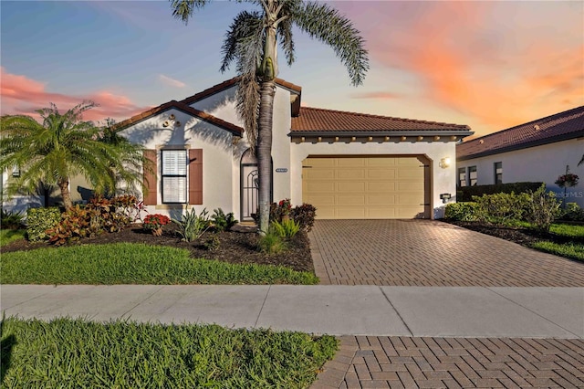 mediterranean / spanish-style home with decorative driveway, a tiled roof, an attached garage, and stucco siding