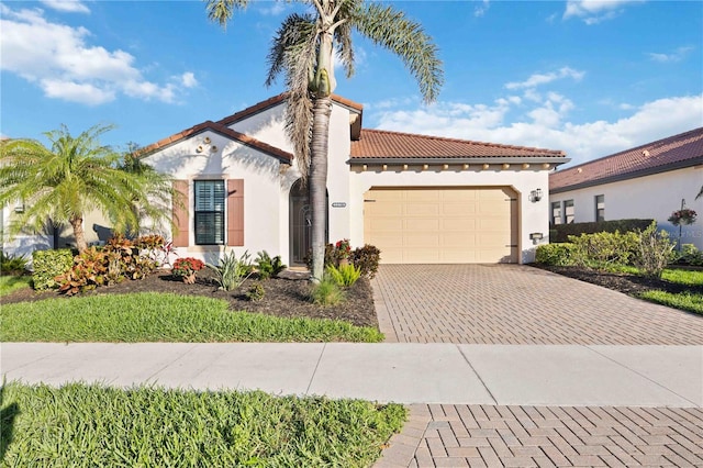 mediterranean / spanish-style house with an attached garage, a tile roof, decorative driveway, and stucco siding