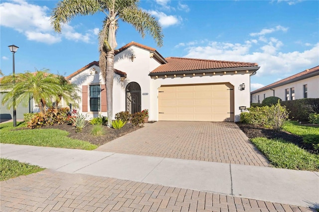 mediterranean / spanish home featuring a garage, a tile roof, decorative driveway, and stucco siding