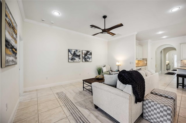 living area with arched walkways, light tile patterned flooring, a ceiling fan, baseboards, and crown molding