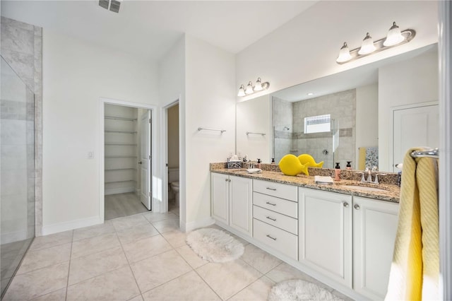 bathroom with double vanity, visible vents, toilet, a sink, and a tile shower