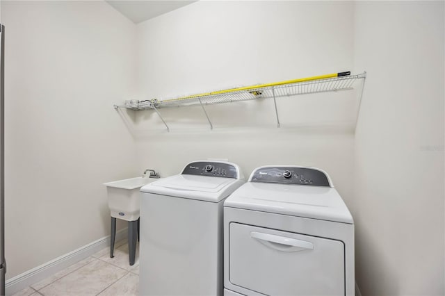 laundry area with light tile patterned floors, a sink, separate washer and dryer, laundry area, and baseboards