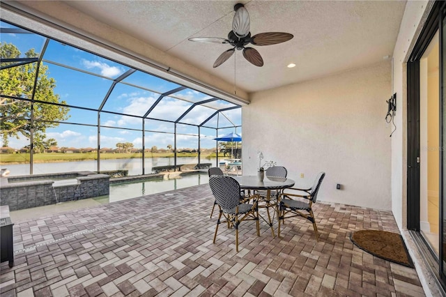 view of patio / terrace with ceiling fan, glass enclosure, outdoor dining space, and a water view