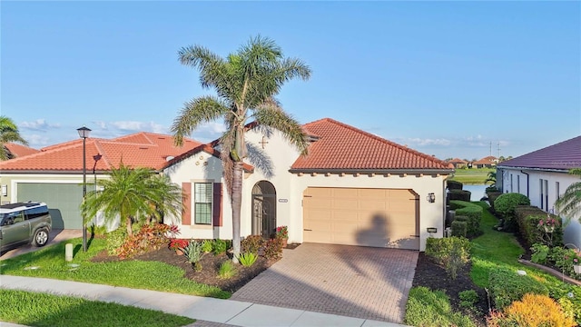 mediterranean / spanish-style home featuring an attached garage, a tile roof, decorative driveway, and stucco siding