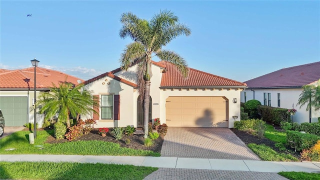 mediterranean / spanish-style home featuring decorative driveway, an attached garage, a tile roof, and stucco siding