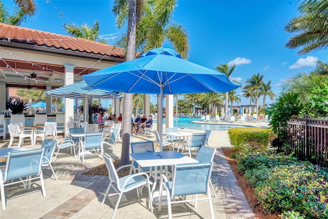 view of patio with a community pool, fence, and a ceiling fan