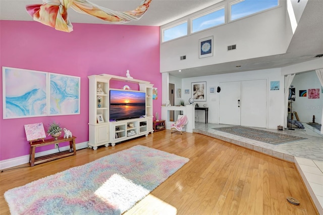 living area with a high ceiling, wood finished floors, visible vents, and baseboards