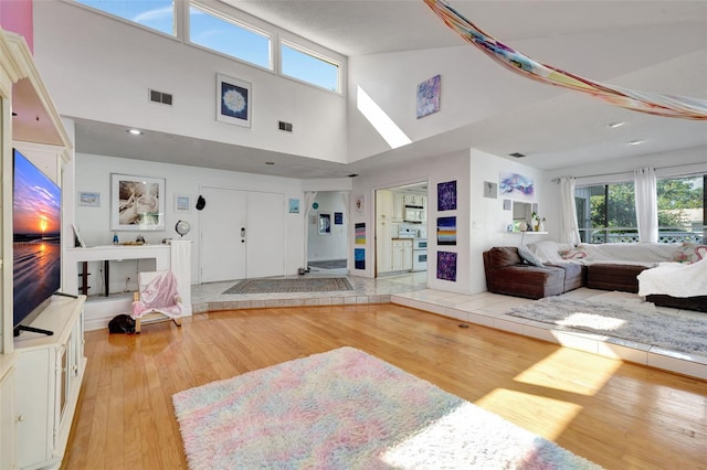 living area with high vaulted ceiling, light wood-type flooring, and visible vents