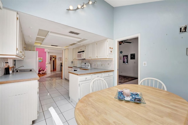 kitchen with white appliances, light countertops, white cabinetry, backsplash, and light tile patterned flooring