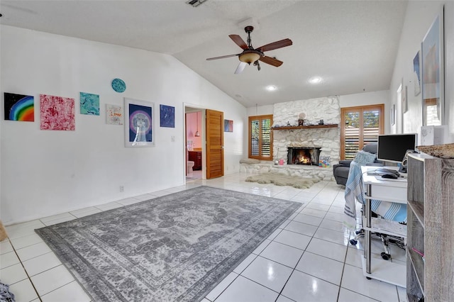 living area with a ceiling fan, vaulted ceiling, a stone fireplace, and light tile patterned floors