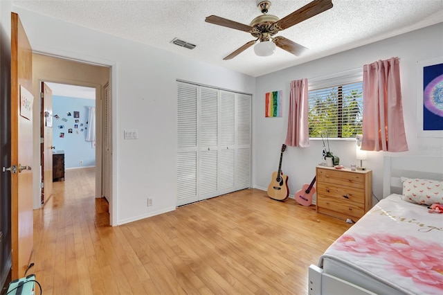 bedroom with baseboards, visible vents, light wood-style flooring, a textured ceiling, and a closet