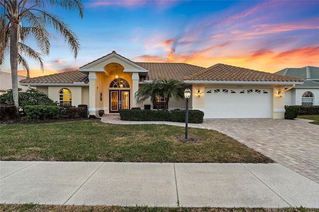 mediterranean / spanish home featuring a garage, french doors, and a lawn