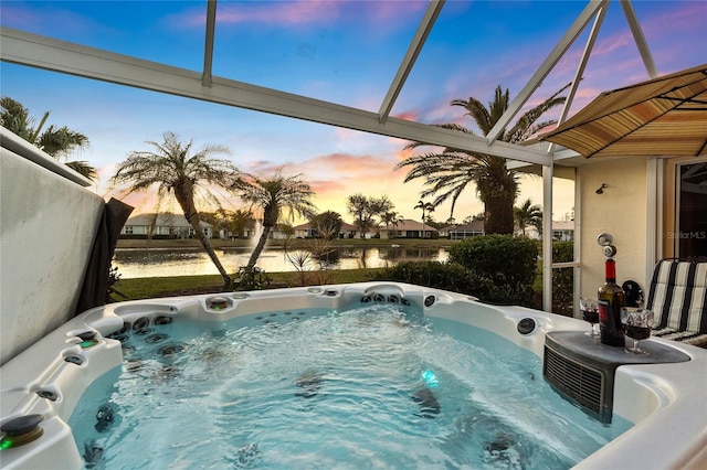 pool at dusk featuring a water view and a hot tub