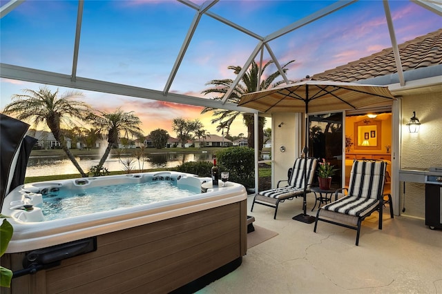 patio terrace at dusk featuring a hot tub, a water view, and glass enclosure