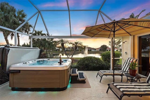 patio terrace at dusk featuring a hot tub, a water view, and glass enclosure