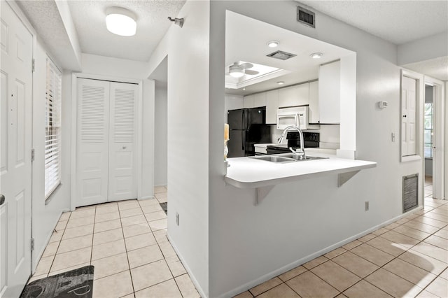 kitchen featuring a kitchen bar, sink, black fridge, a textured ceiling, and white cabinets